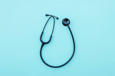 Açık mavi arka planda siyah modern steteskop. Tıp ve sağlık, kardiyoloji, tıp eğitimi. Akustik tıbbi cihaz. Mesaj için yer var. Düz-yatay, üst görünüm.