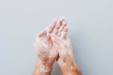 El yıkama konsepti. Adam ellerini gri arka planda sıvı dezenfektan sabunla temizliyor. Uzayı kopyala Düz-Yat. Kişisel hijyen ve Coronavirus önleme.