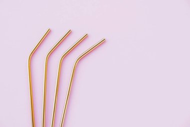 Modern, yeniden kullanılabilir, pastel pembe arka planda, yüksek açılı, çevre dostu altın pipetler. Mesajlaşmak için alan, düz-yatış. Sıfır atık ve sürdürülebilir yaşam tarzı kavramı.