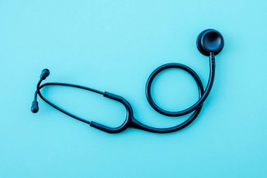 Açık mavi arka planda siyah modern steteskop. Tıp ve sağlık, kardiyoloji, tıp eğitimi. Akustik tıbbi cihaz. Mesaj için yer var. Düz-yatay, üst görünüm.