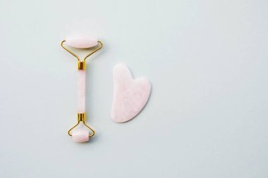 Pembe kuvarstan yapılmış yeşim taşı silindirli, lenfatik drenaj yüz masajı için doğal bir alet. Üst görünüm gri arkaplan, kopyala boşluk, kapat. Güzellik ve vücut bakımı.