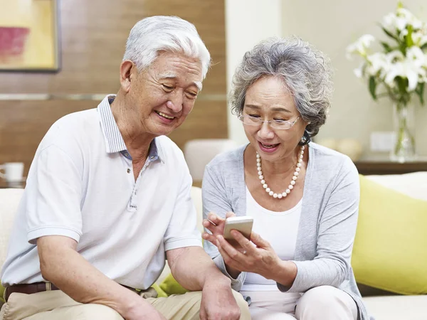 Sênior asiático casal usando celular em casa — Fotografia de Stock