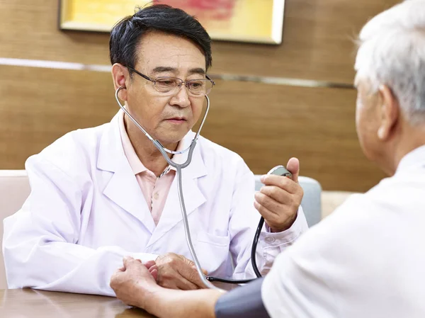 Medico asiatico controllando la pressione sanguigna di un paziente anziano — Foto Stock