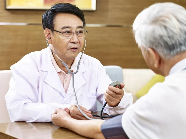 Asiático médico verificando a pressão arterial de um paciente sênior — Fotografia de Stock