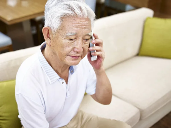 Грустный старший азиатский мужчина разговаривает по мобильному телефону — стоковое фото