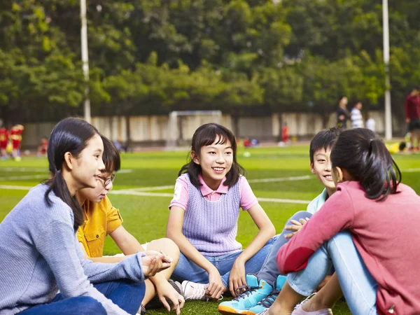 앉아서 잔디에 채팅 아시아 초등 학생 — 스톡 사진