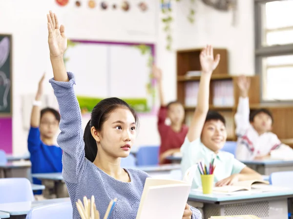 Asian pupil raising hands in classroom — Stock Photo, Image