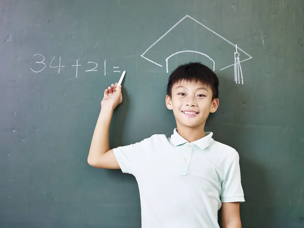 asian elementary schoolboy standing under a chalk-drawn doctoral cap