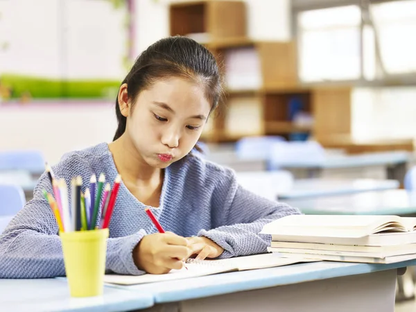 Asian elementary schoolgirl doing homework in classroom — Stock Photo, Image