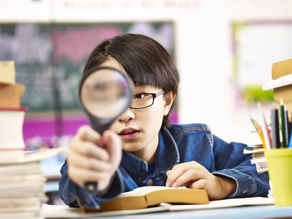 Nyfiken asiatisk elev håller ett förstoringsglas framför ena ögat — Stockfoto