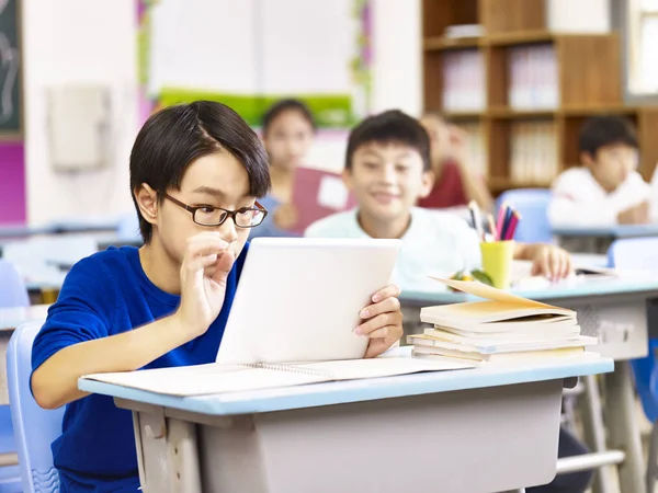 Asiático escuela primaria estudiante usando tableta en aula — Foto de Stock