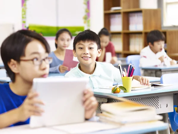 Asiático escuela primaria estudiante usando tableta en aula — Foto de Stock