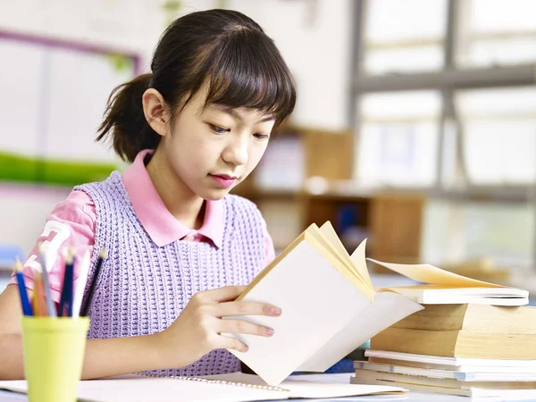 Asian pupil reading a book in classroom — Stock Photo, Image