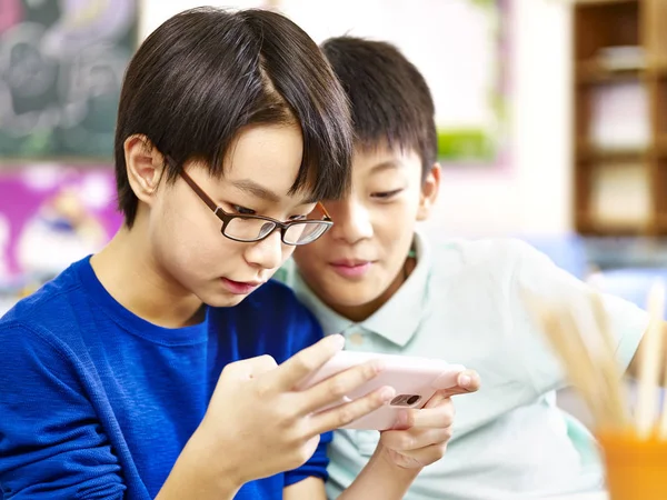 Dos asiático elemental colegiales jugando juego con celular —  Fotos de Stock