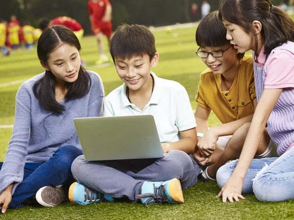 Asiático primaria escuela niños usando laptop al aire libre —  Fotos de Stock