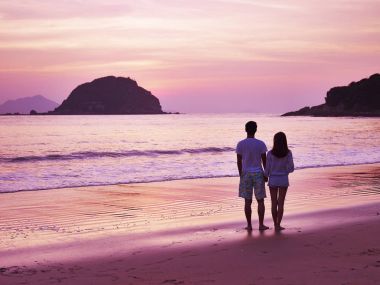 gün doğmadan önce kumsalda yürüyen genç Asyalı Çift