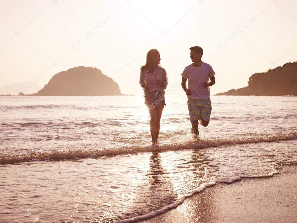 young asian couple running on beach