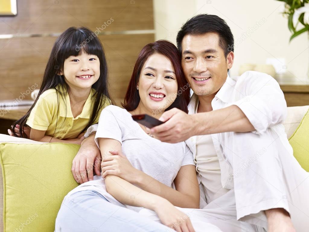 asian parents and daughter watching TV at home