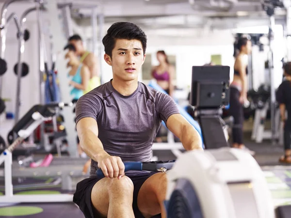 Asian young man working out on rowing machine — Stock Photo, Image