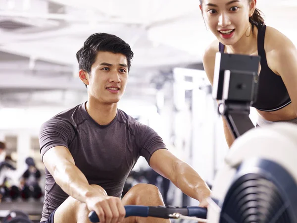 Joven asiático pareja trabajo fuera usando remo máquina — Foto de Stock