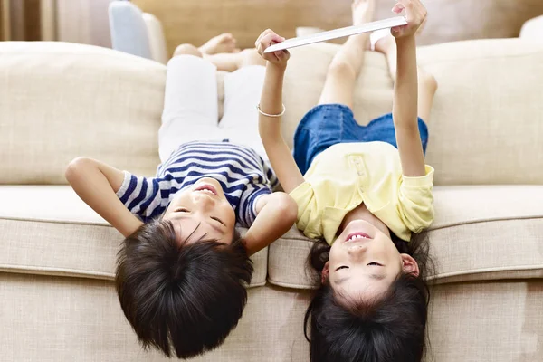 Dvě asijské malý děti ležící hlavou dolů na gauči — Stock fotografie