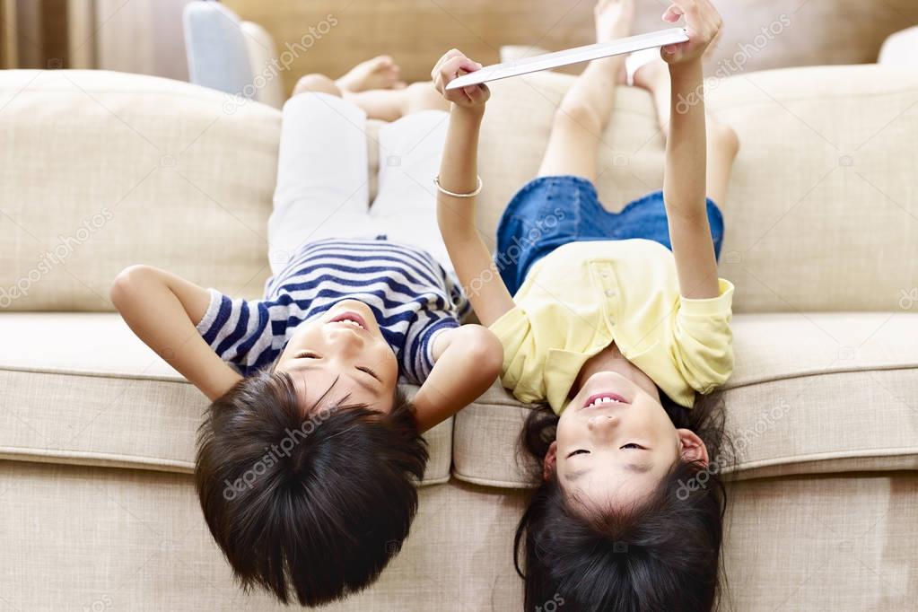 two asian little kids lying upside down on couch