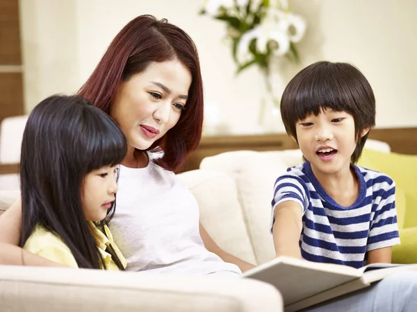 Mãe asiática e duas crianças lendo um livro em casa — Fotografia de Stock