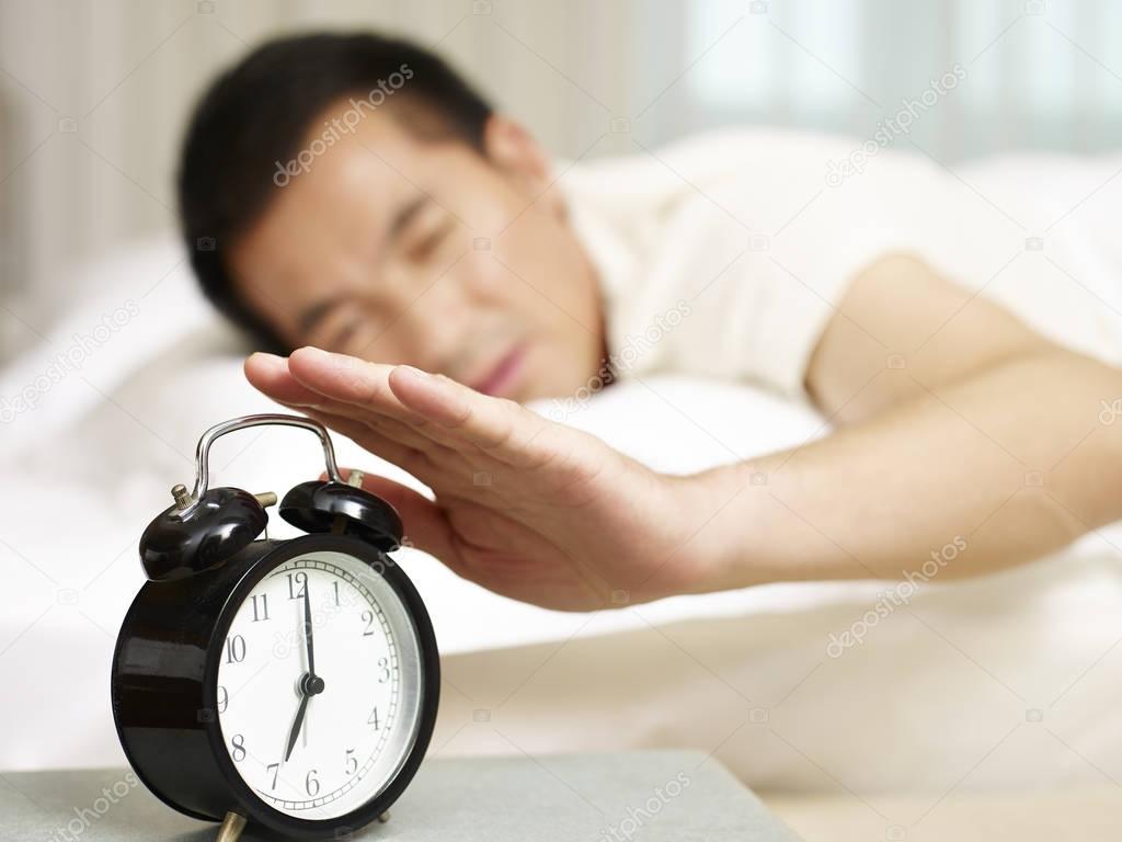 asian man trying to stop alarm clock