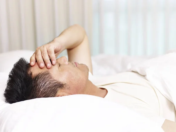 Asian man lying on bed hand on forehead — Stock Photo, Image