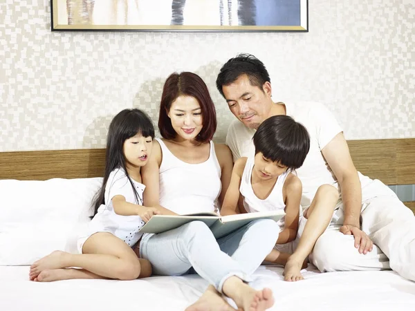 Asiatisches Paar und zwei Kinder lesen gemeinsam Buch im Bett — Stockfoto