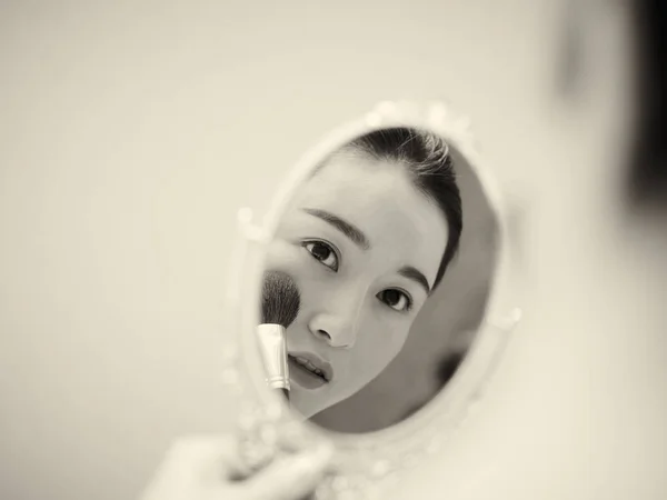 Νεαρά ασιατικές γυναίκα κοιτάζοντας εαυτό στον καθρέφτη ενώ εφαρμογή make- — Φωτογραφία Αρχείου