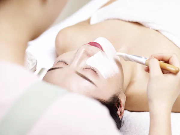 Asiatische Kosmetikerin Anwendung Gesichtsmaske auf Gesicht der jungen Frau — Stockfoto