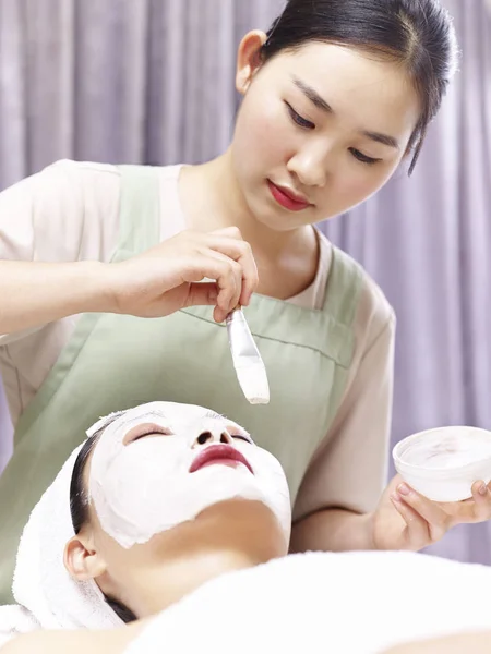 Asiatice cosmetician aplicarea masca facială pe fata de femeie tânără — Fotografie, imagine de stoc