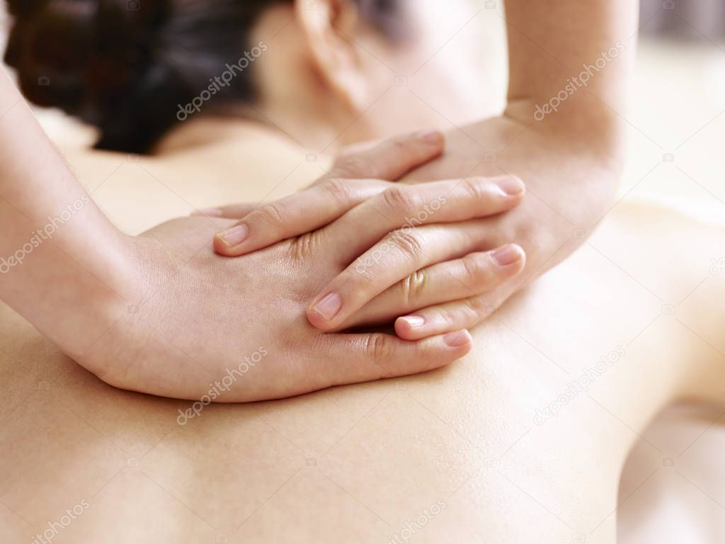 hands of masseur performing massage on young asian woman