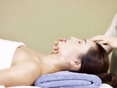young asian woman receiving face massage in spa salon clipart