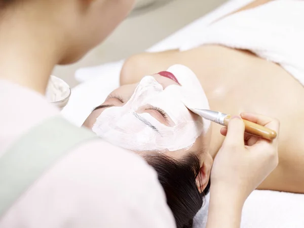 Азиатский косметолог наносит маску на лицо молодой женщины — стоковое фото