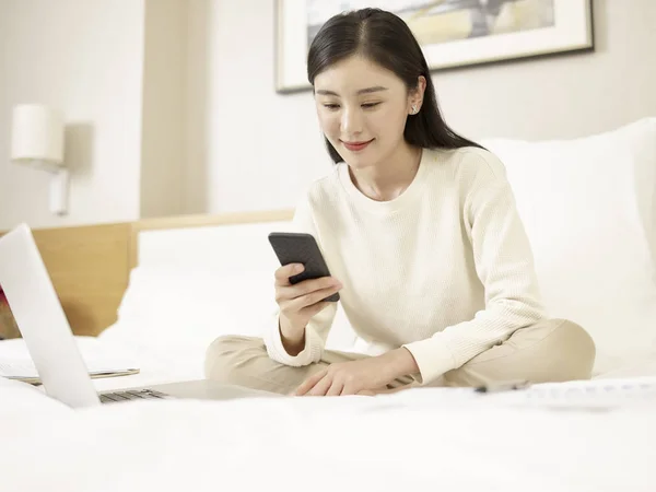 Joven asiático mujer usando celular y portátil en cama —  Fotos de Stock