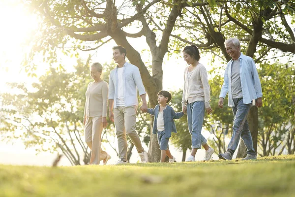 Üç kuşak Asyalı aile parkta yürüyor.