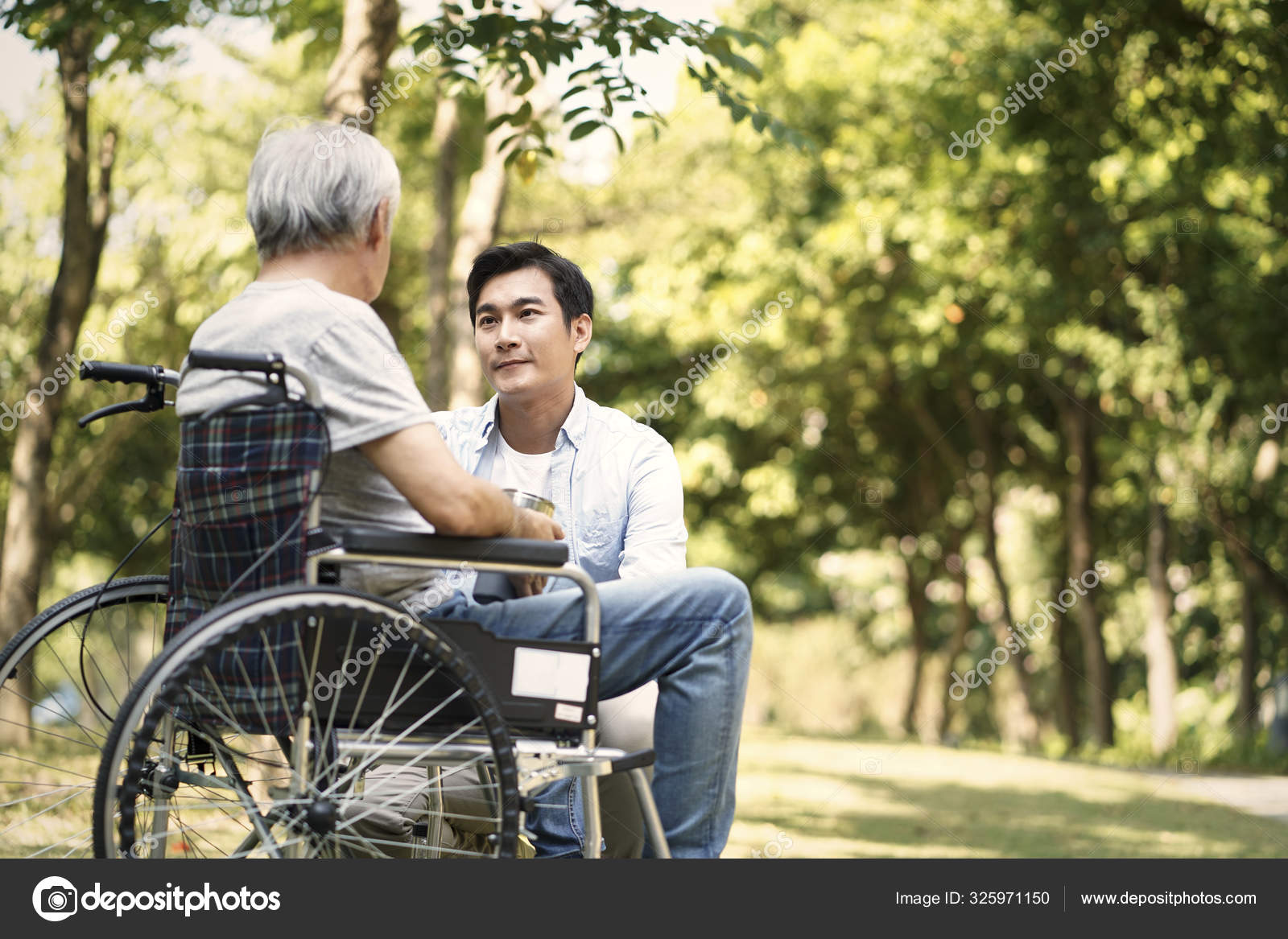 Asian Son Comforting Wheelchair Bound Father Stock Photo