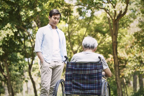 Азіатський син розмовляє з прив'язаним батьком інвалідного візка — стокове фото