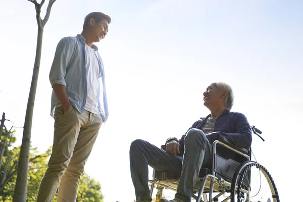 Asian son talking to wheelchair bound father — Stock Photo, Image