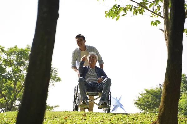 Asian son and wheelchair bound father enjoying nature — Stock Photo, Image