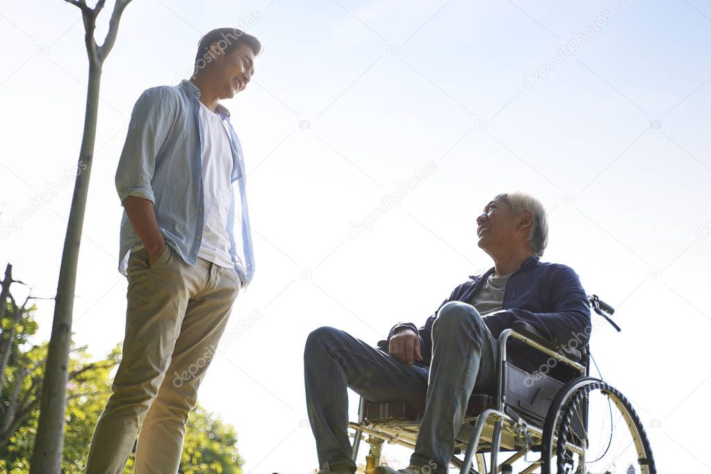 asian son talking to wheelchair bound father