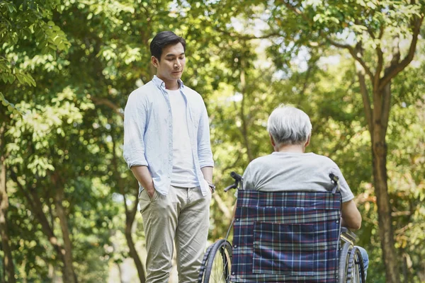 Asian son talking to wheelchair bound father — Stock Photo, Image