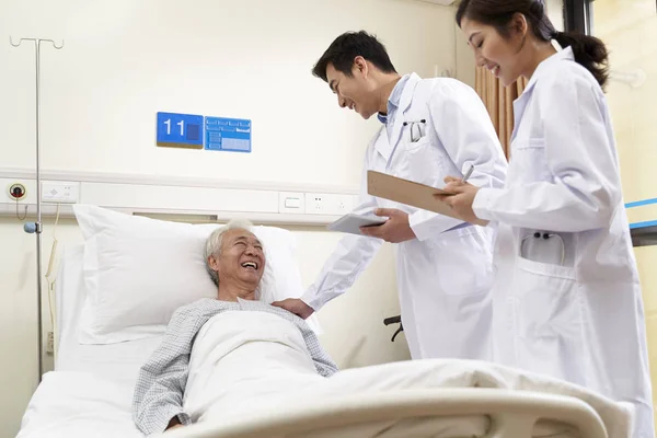 Two young asian doctors talking old man at bedside — Stock Photo, Image