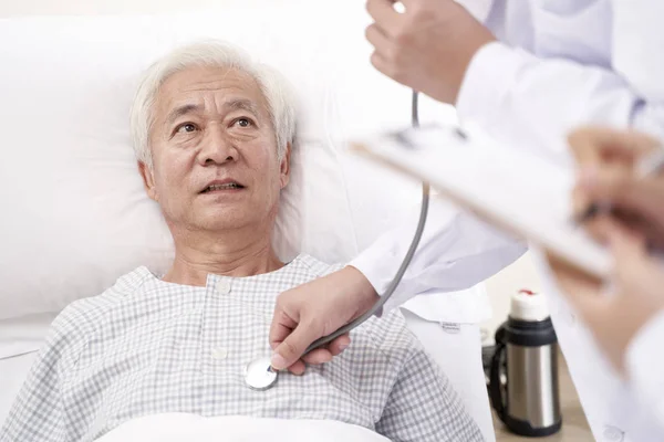 Asiatisk äldre patient som ligger i sängen och undersöks av läkare i — Stockfoto