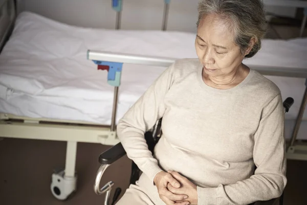 Triste asiático velho mulher sentado em cadeira de rodas ao lado de hospital cama — Fotografia de Stock