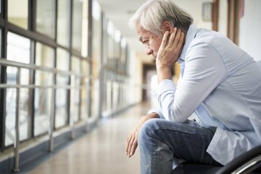 devastated senior asian man sitting in hospital hallway