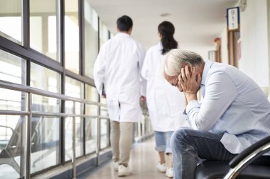 devastated senior asian man sitting in hospital hallway