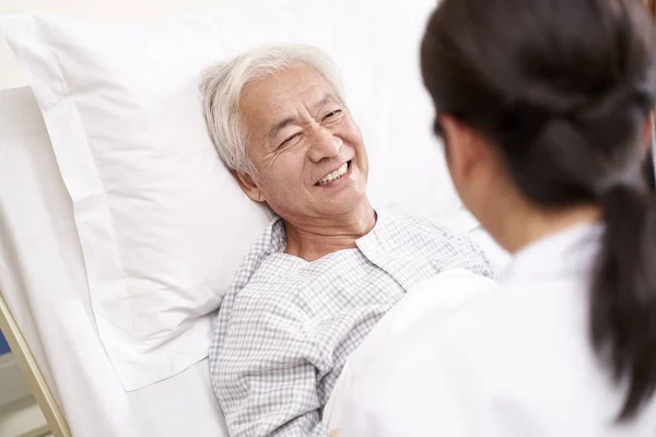 Fiatal ázsiai orvos beszél idős beteg az ágy mellett hospt — Stock Fotó